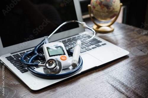 Technology and medicine - Silver stethoscope and blood glucose meter over laptop keyboard. Concept of healthcare medical and check up, diabetes, glycemia.