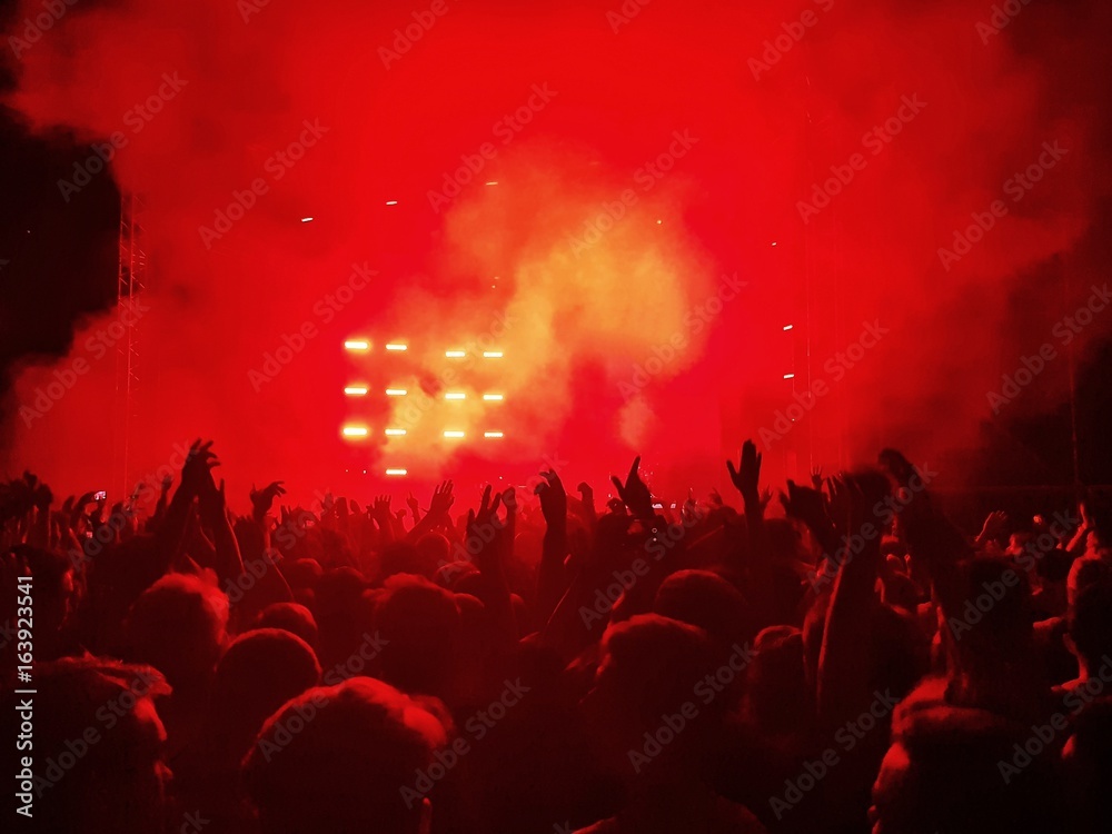A crowd with their hands up in the air under the scene in red smoke