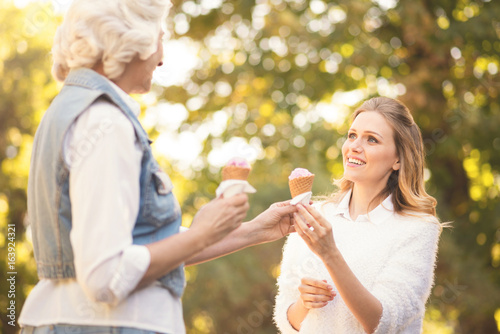 Amused young woman tasting ice cream with aged mother outdoors