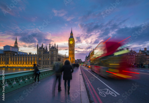 London, England - Iconic Red Double Decker Bus on the move on Westminster Bridge with Big Ben and Houses of Parliament at background. Sunset with beautiful colorful sky