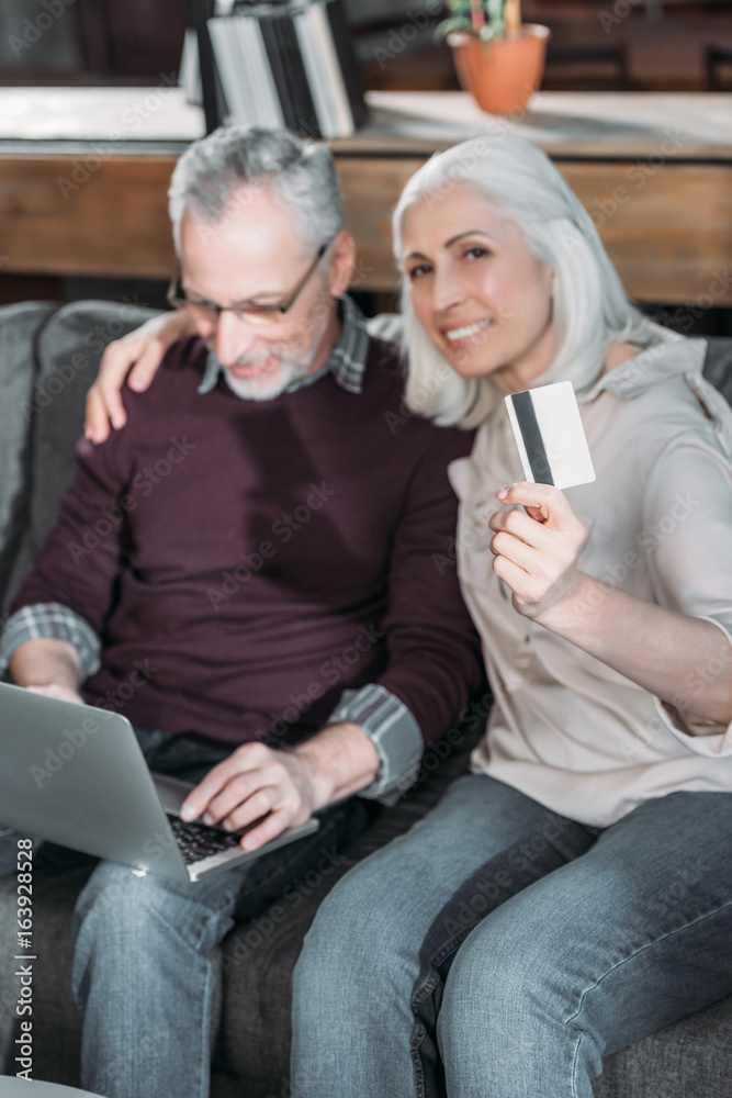 senior couple buying goods online while sitting on sofa at home