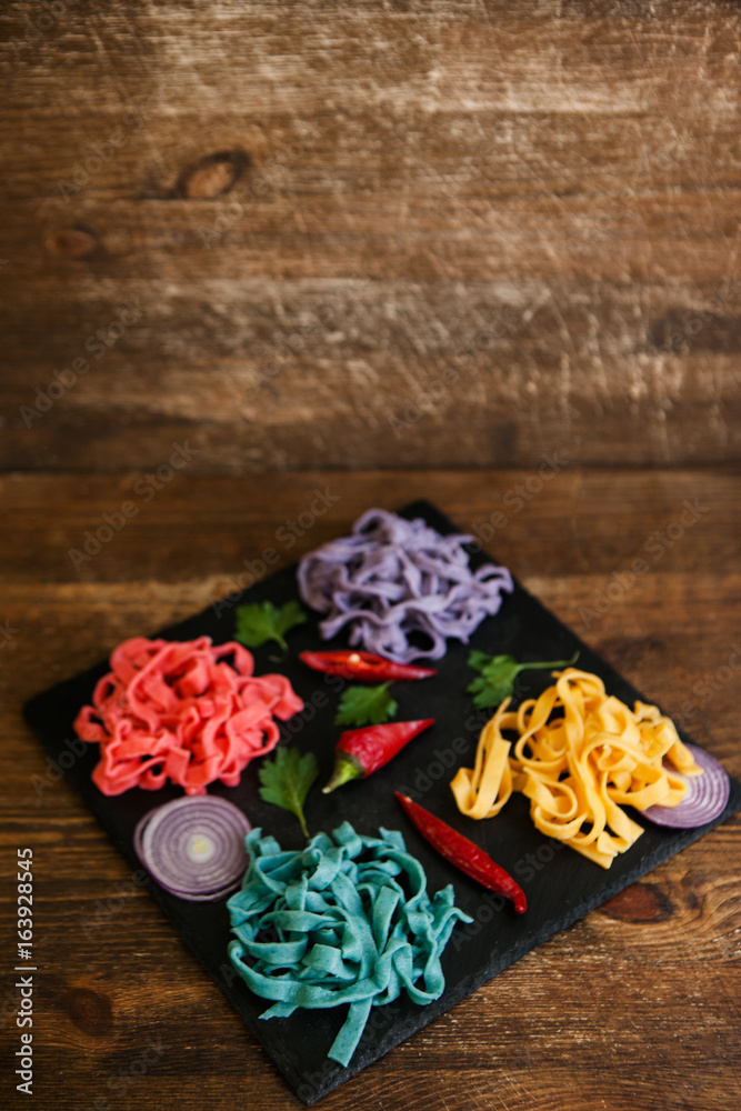 Colorful pappardelle with spices on black plate on table. Food concept top view, background with free space Colorful pappardelle with spices on black plate on table. Food concept top view, background with free space