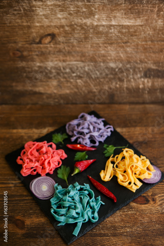 Colorful pappardelle with spices on black plate on table. Food concept top view, background with free space