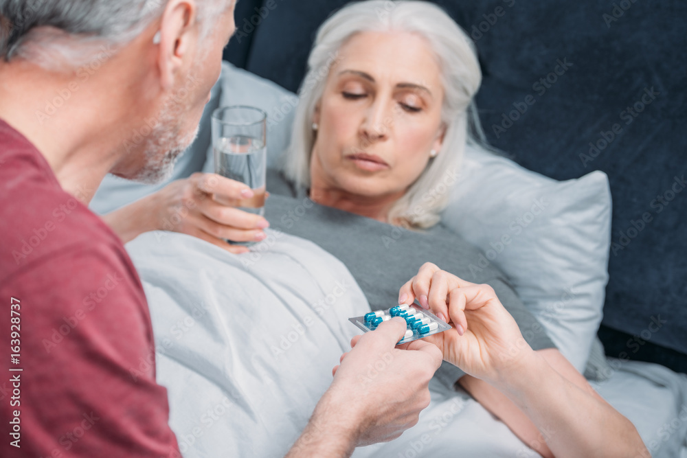 man giving medicines to sick senior wife in bed