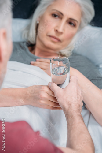 man giving glass of water to sick wife in bed