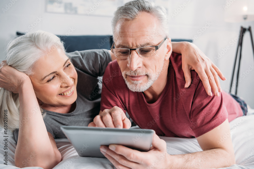 happy senior couple with digital tablet resting in bed together