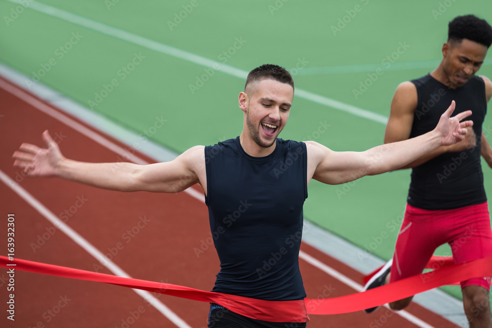 Cheerful young athlete man crossing finish line