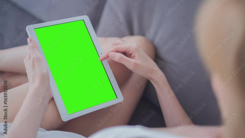 Young Woman in white top laying on couch uses Tablet PC with pre-keyed green screen. Few types of gestures - scrolling up and down, tapping, zoom in and out. Perfect for screen compositing Young Woman in white top laying on couch uses Tablet PC with pre-keyed green screen. Few types of gestures - scrolling up and down, tapping, zoom in and out. Perfect for screen compositing