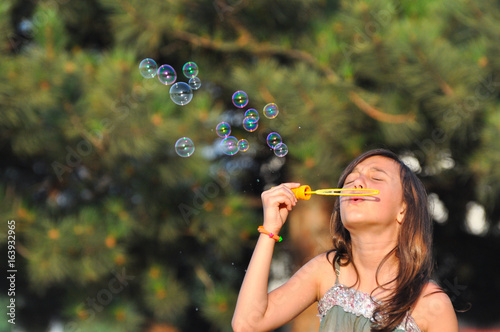 Adorable girl blowing soap bubbles in summer park. Girl play in park and blowing soap bubbles