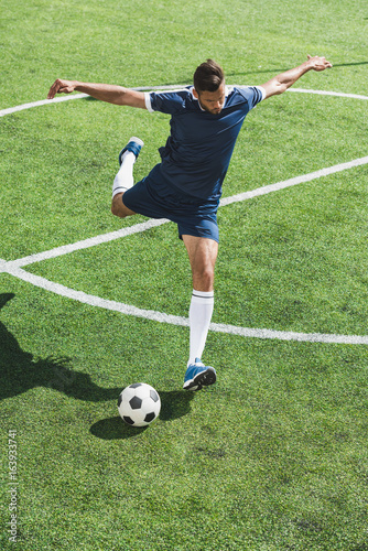 athletic soccer player kicking ball on soccer pitch