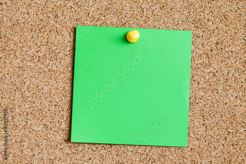 Cork board with green memo reminder card attached with yellow pin. 