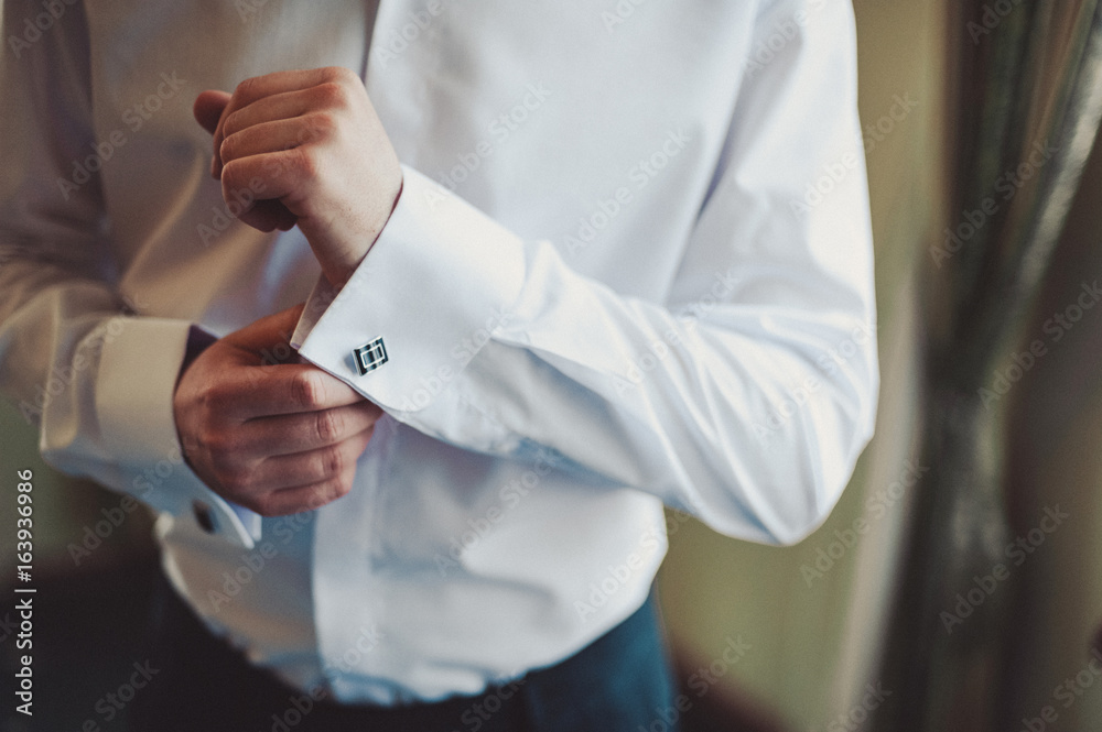 The groom fastens the cufflink on the shirt sleeve close-up