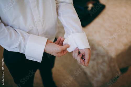 The groom fastens the cufflink on the shirt sleeve close-up