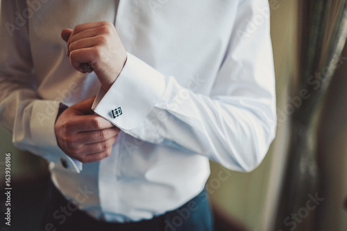The groom fastens the cufflink on the shirt sleeve close-up