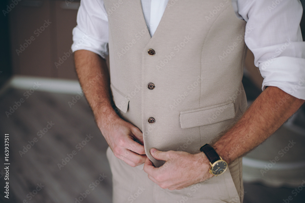 Elegant groom in wedding jacket wearing white shirt and turquoise tie. Groom's hands on blue suit. Elegant groom in wedding jacket wearing white shirt and turquoise tie. Groom's hands on blue suit.