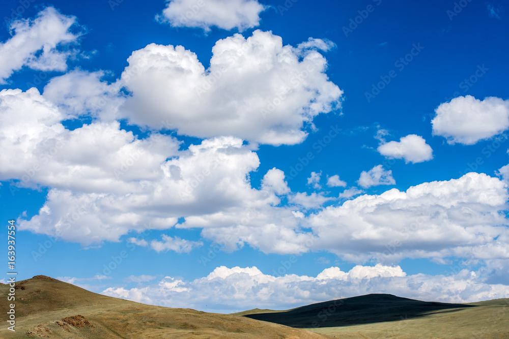shadows of fluffy clouds over green hills at sunny day  
