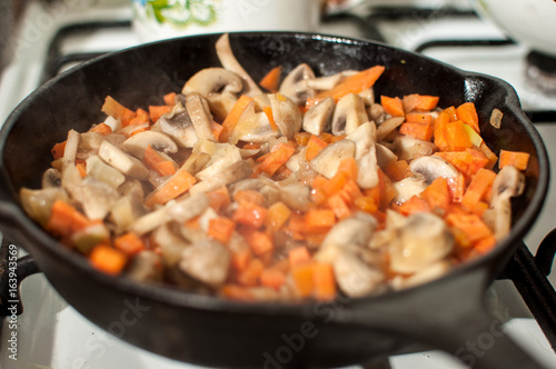Delicious fried mushrooms champignons, carrot and onion in pan on gas stove