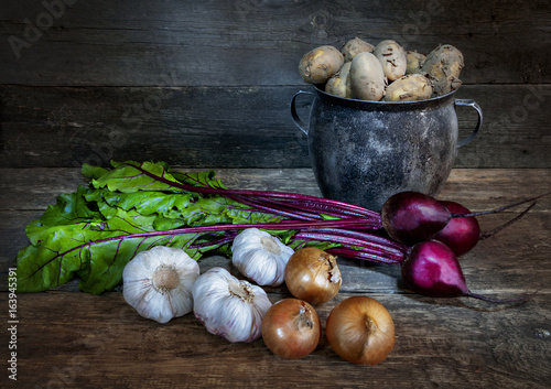 An old pot potato onion garlic beetroot on old board background photo