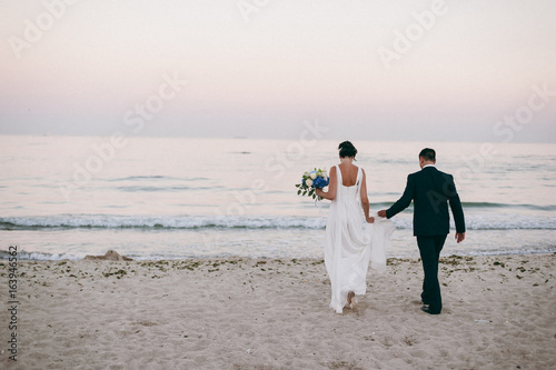 Wedding couple on a walk bride and groom sea field sunset architecture grass sand © ViDi Studio