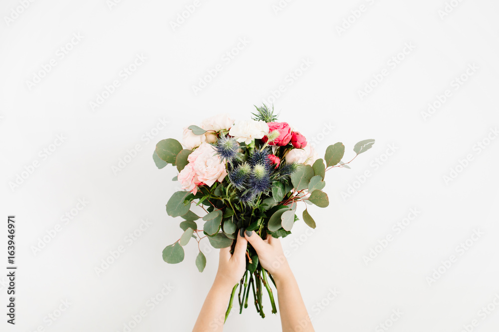 Naklejka premium Girl's hands holding beautiful flowers bouquet: bombastic roses, blue eringium, eucalyptus, isolated on white background. Flat lay, top view. Floral composition