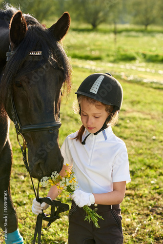 Fotografie Pretty little girl jockey communicating with her black horse in professional out
