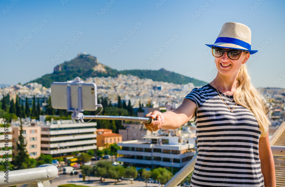 Beautiful young girl shoots selfie on a mobile phone on a rest by the landmark.