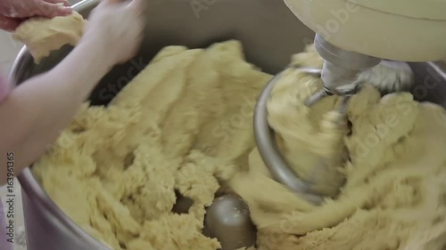 Preparation of dough using automatic mixer under control of worker in bakeryhouse. Homogeneous mixture formed by mixing flour with other natural ingredients such as water, yeast, sugar, oil, eggs in photo