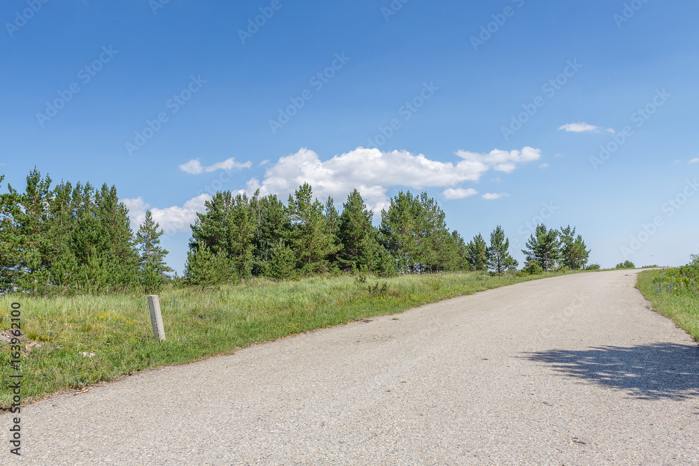 Road in mountain forest sky with white clouds in East Kazakhstan Region.
