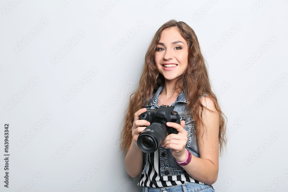 Portrait of young woman with camera on grey background