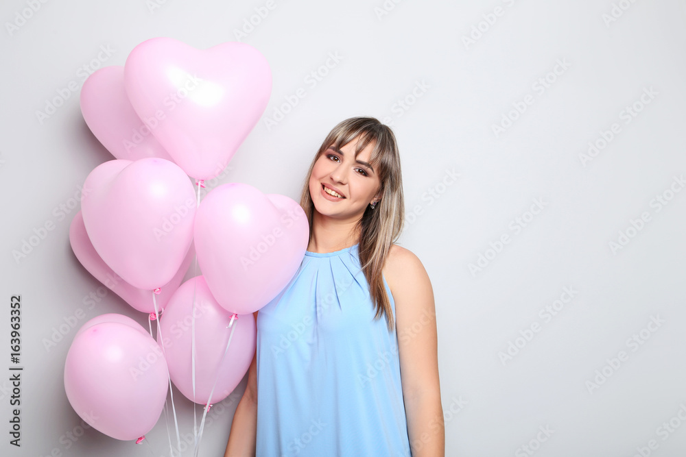 Portrait of young woman with pink heart balloons on grey background Portrait of young woman with pink heart balloons on grey background