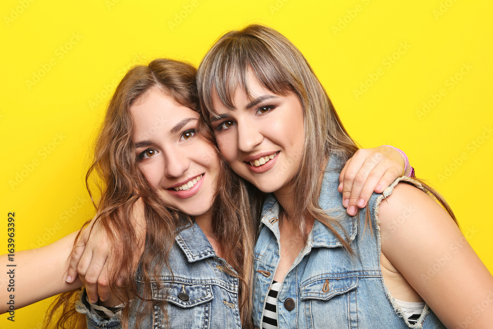Two young woman hugging each other on yellow background Two young woman hugging each other on yellow background