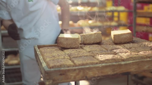 Rotation view of just baked steaming loaves of bread being put by young baker onto the cooling rack. Delicious atmosphere, place of work.
