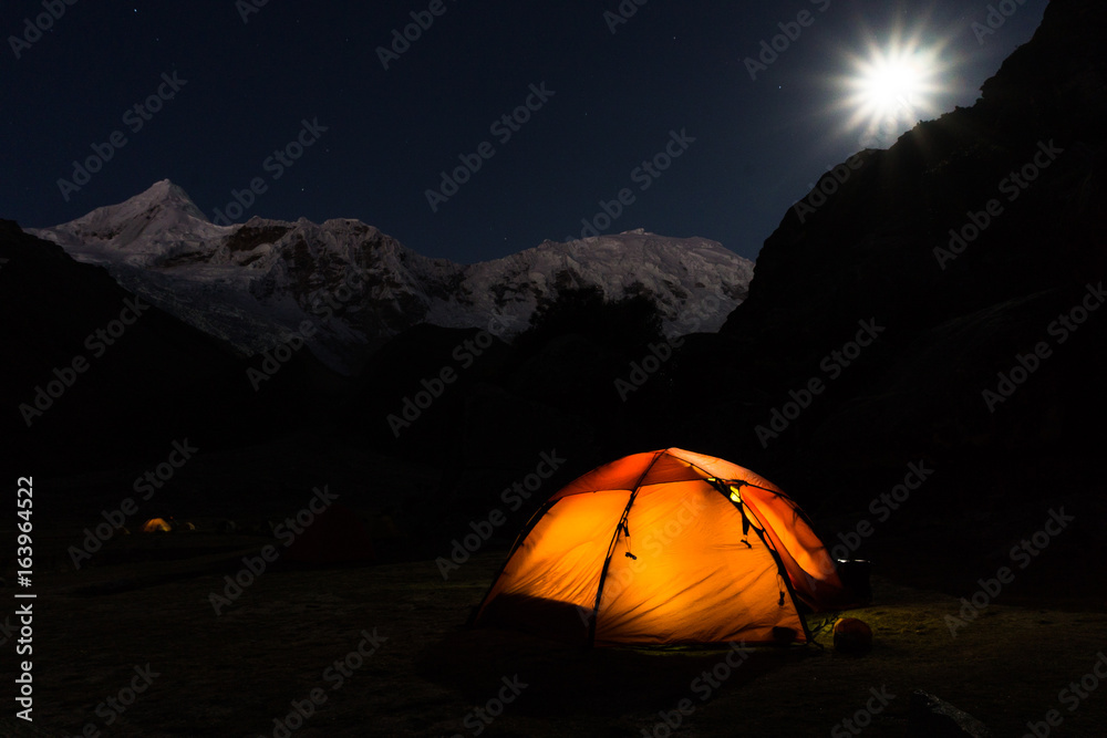 glowing orange tent at night at a campsite in the Andes in Peru under a full moon with mountains in the background