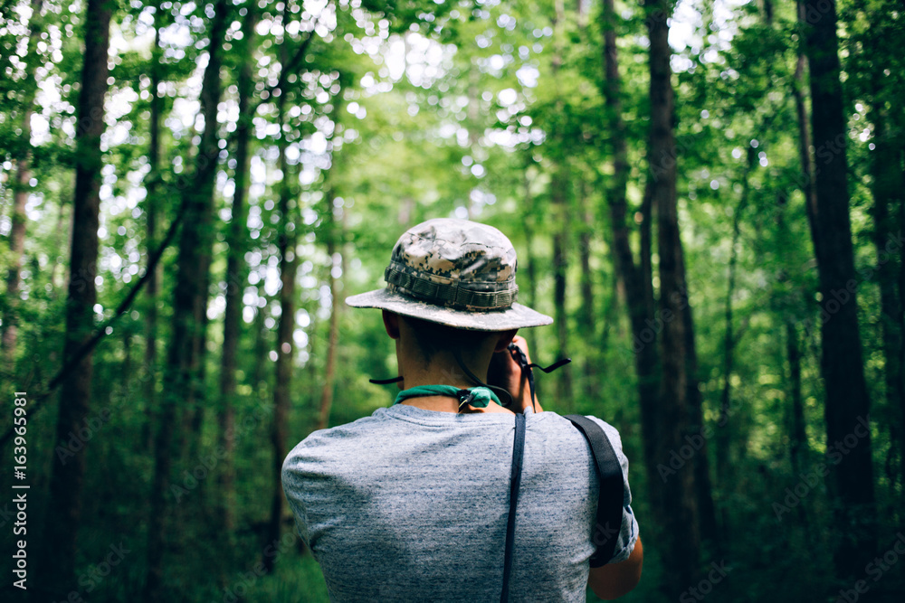 Photo from the back of hipster nomad adventurer exploring exotic forest in national park wears a panama hat and makes photos of inspirational nature Photo from the back of hipster nomad adventurer exploring exotic forest in national park wears a panama hat and makes photos of inspirational nature