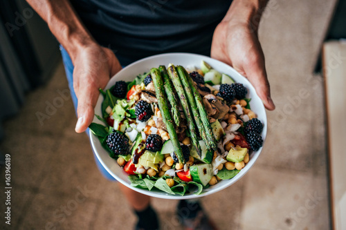 Man hands holding big deep plate full of healthy paleo vegetarian salad made from fresh organic biological ingridients, vegetables and fruits, berries and other nutritional things photo