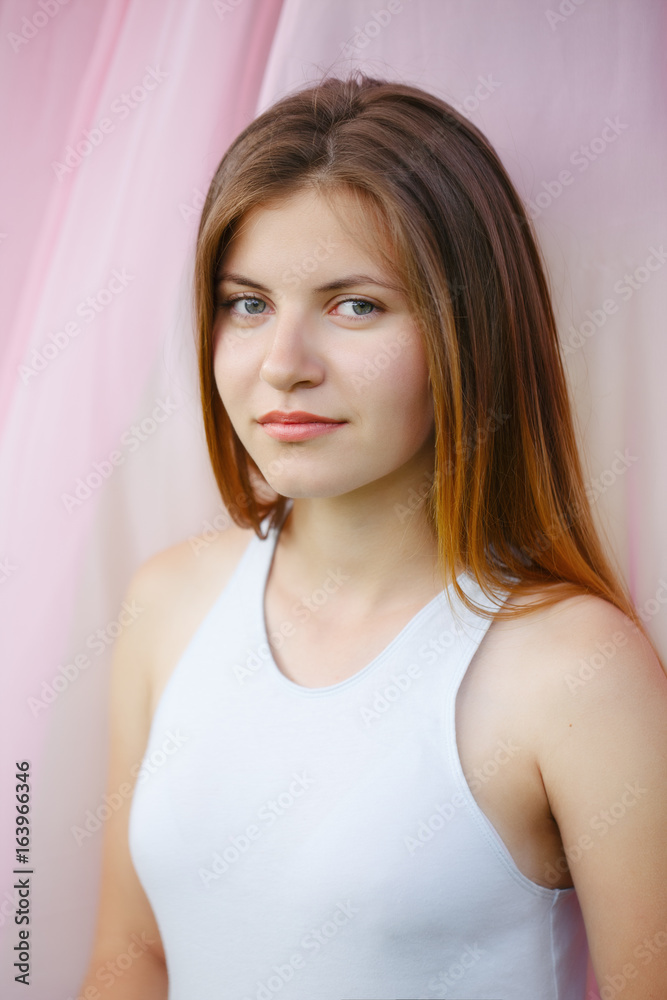 Closeup portrait of beautiful smiling young Caucasian woman with long red hair in white t-shirt relaxing in park on pink background, looking in camera. Beauty and skin care. Youth and happiness. Closeup portrait of beautiful smiling young Caucasian woman with long red hair in white t-shirt relaxing in park on pink background, looking in camera. Beauty and skin care. Youth and happiness.