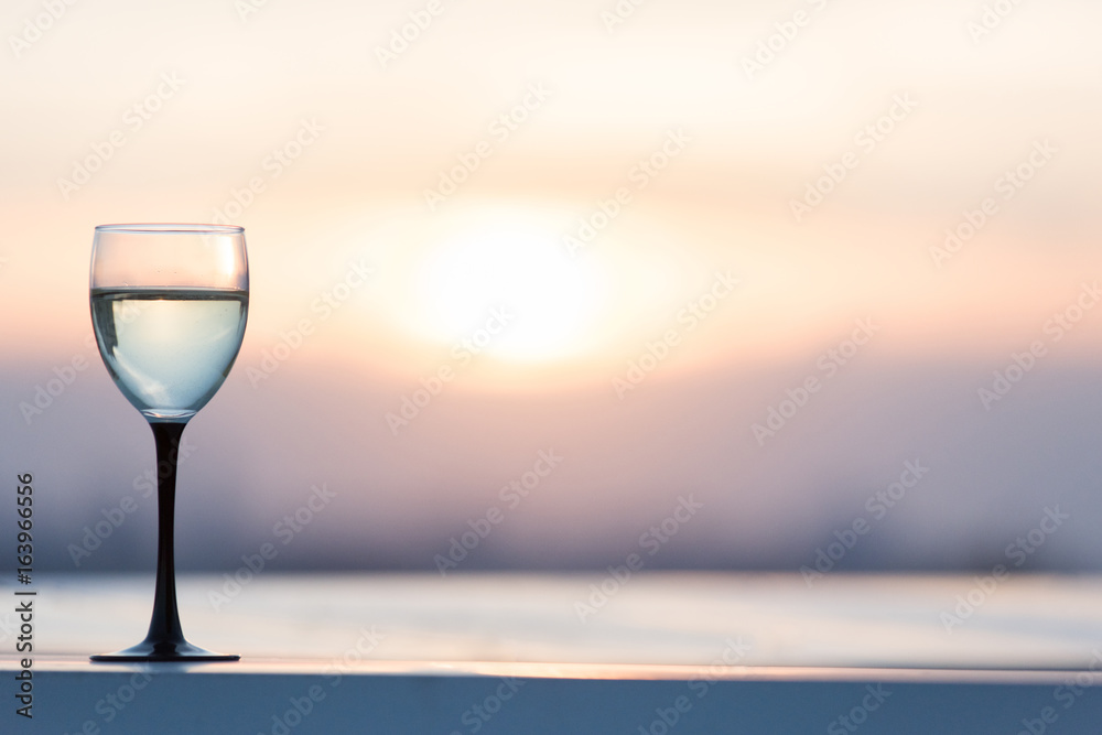 A glass with a white wine in the light of the setting sun. Vibrant alcohol background.
