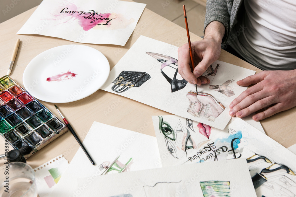 Fashion sketch designed by artist. Unrecognizable person makes a design of footwear model among other drawings of fashion models around Fashion sketch designed by artist. Unrecognizable person makes a design of footwear model among other drawings of fashion models around