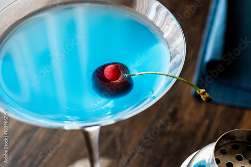 Blue Moon Cocktail with cherry on wooden surface.
