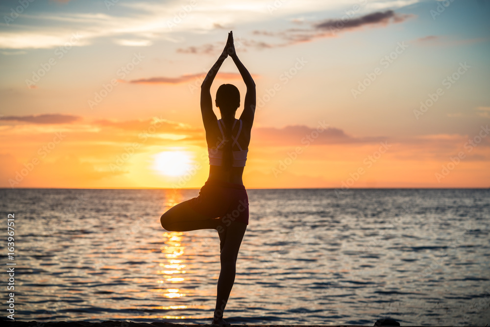 Fit woman practicing the yoga tree pose for a toned body on an idyllic beach at sunset