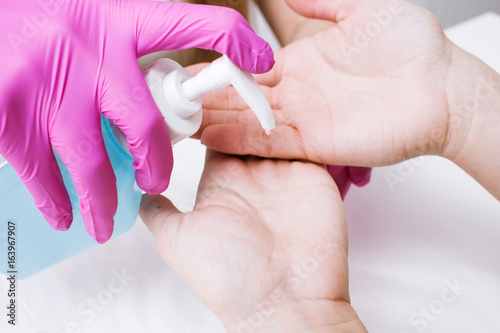 Disinfection hands before manicure in the salon closeup. Beautician is disinfecting client's with desinfectant photo