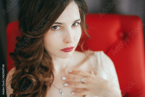 Young beautiful bride sitting on armchair and waiting for her groom