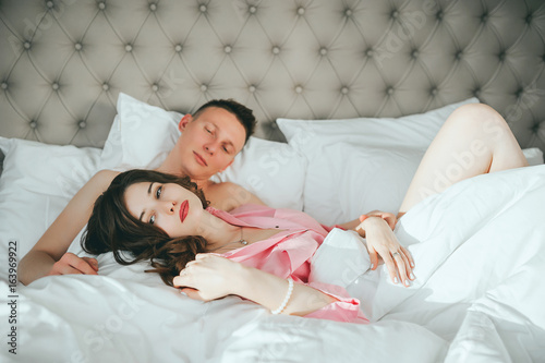Fashion photo of two young beautiful lovers relax at the hotel on a bed,they are smiling photo