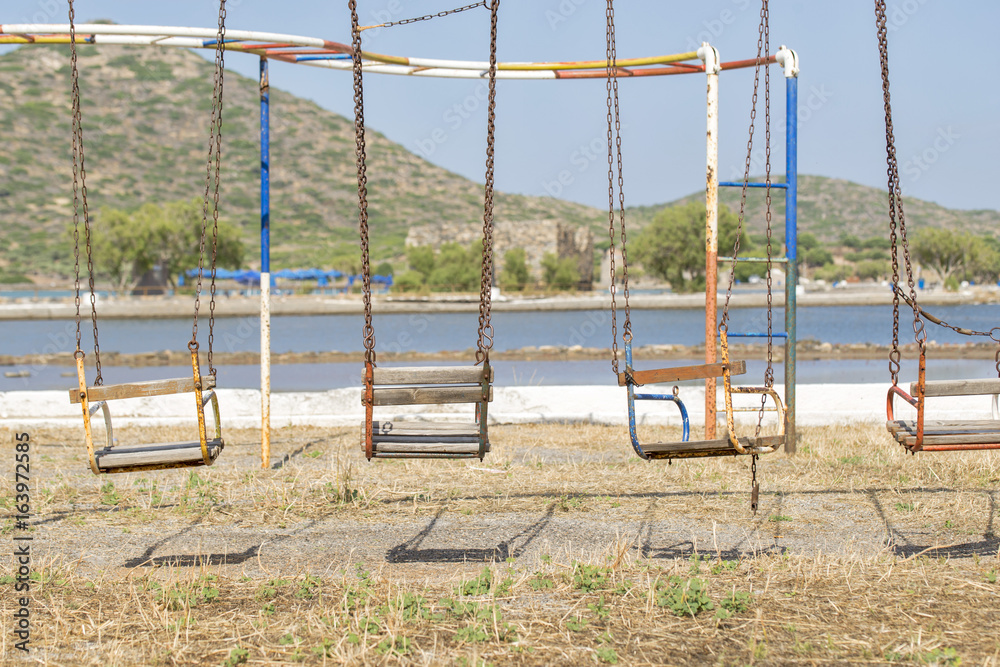 old swings in playground near the sea and mountain