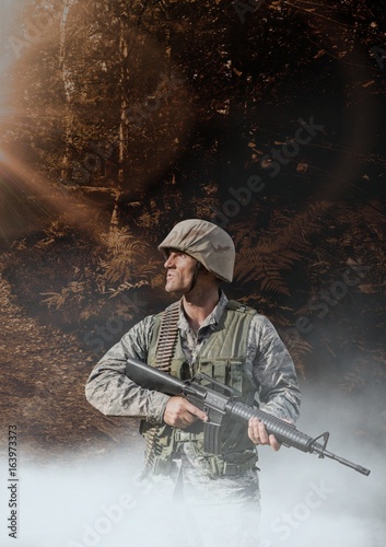 Soldier man holding a weapon against woods