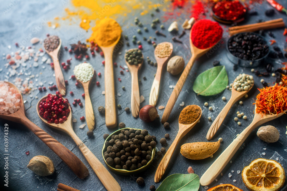 Various indian spices in wooden and silver spoons and metal bowls, seeds, herbs and nuts on dark stone table. Colorful spices, selective focus. Organic food, healthy lifestyle.
