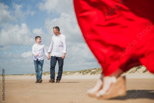 Happy father walks with his son on the coast of sea and mother goes to them photo