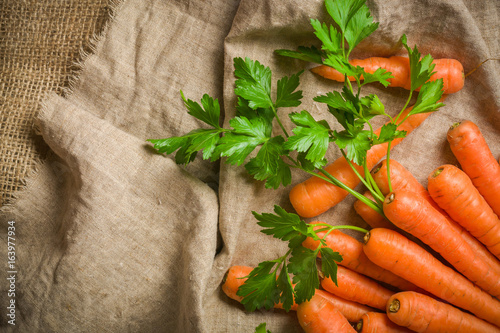 Carrots of various sizes stacked in a pile on a burlap background. Washed and ready to eat. View from above