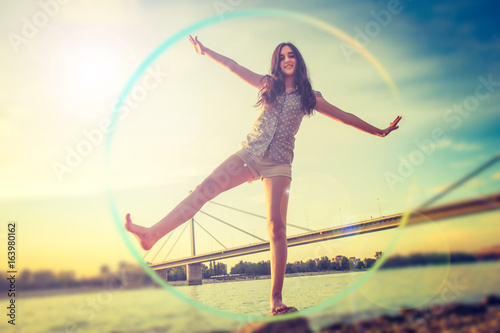 Teenage girl balancing on the stone while the sun sets / Cheerful teenage girl balancing on the beach photo