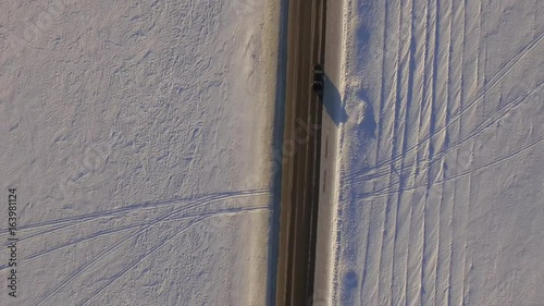 Aerial view of snowy fields and road. SUV driving on winter roads through the snowy field. Aerial view of the car driving on road and the fields in the winter photo